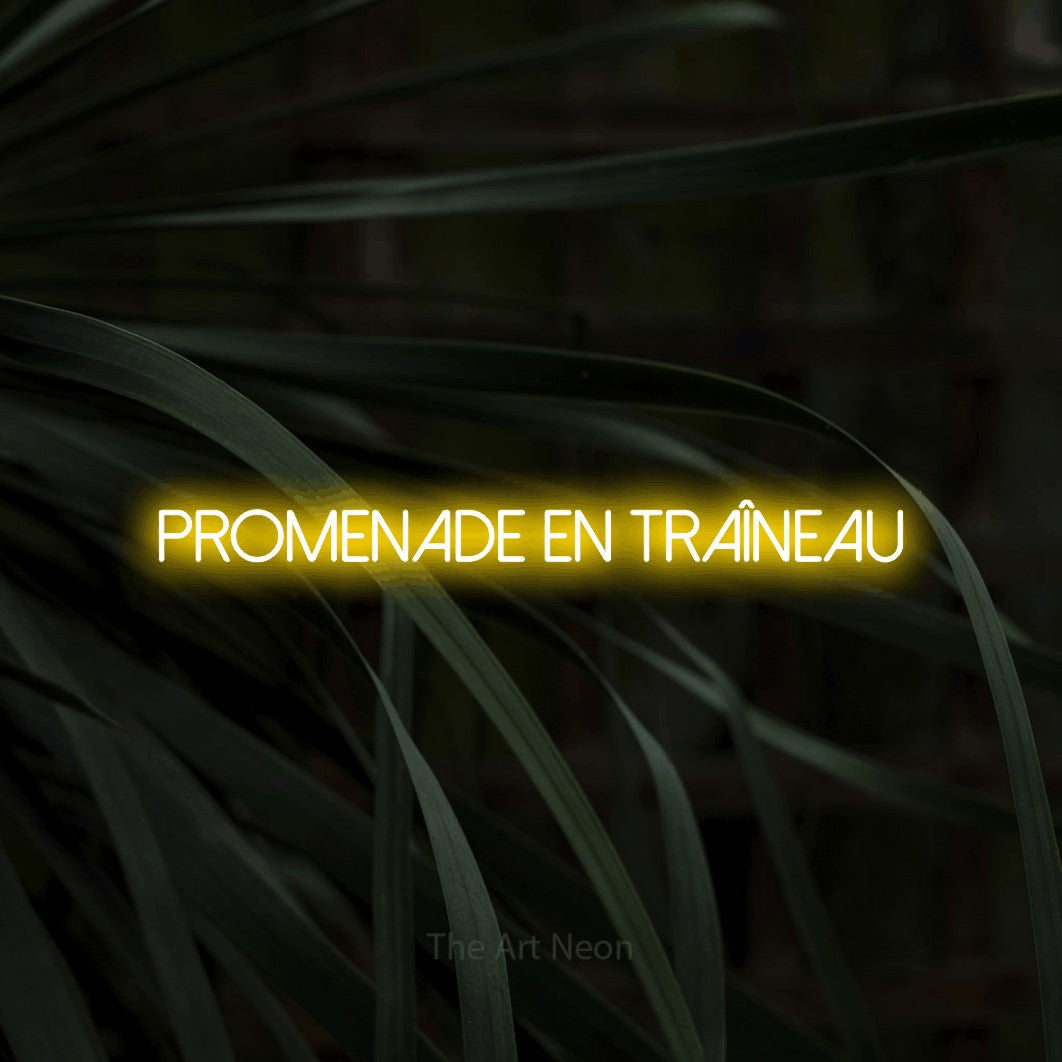“Promenade en traîneau” LED neon sign in yellow, with thin sans-serif lettering, shown against a close-up of dark foliage.