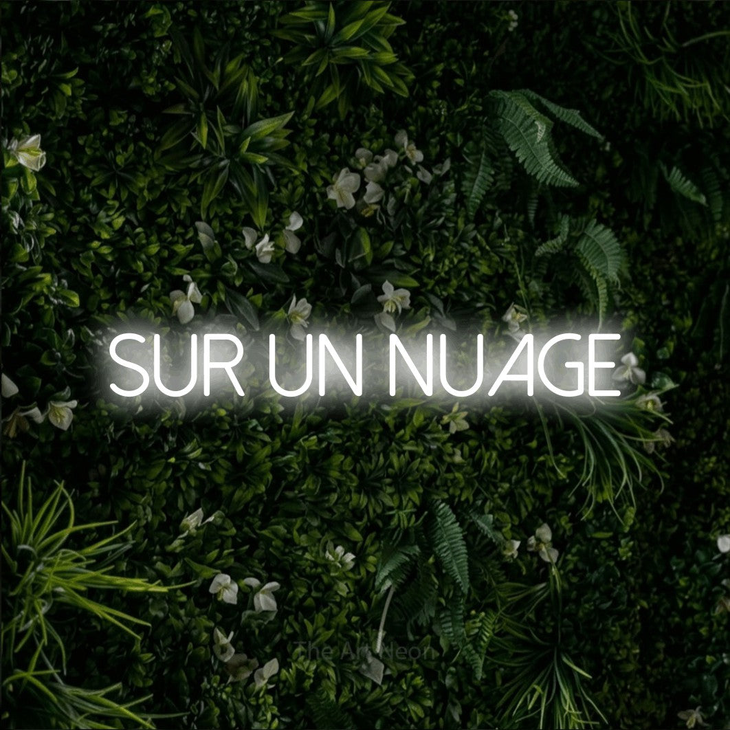 “Sur un nuage” LED neon sign in cool white, with thin sans-serif lettering, shown against a dense green plant wall.