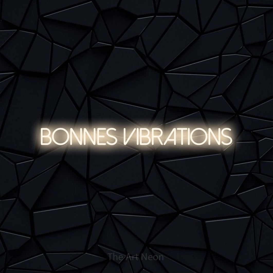 “Bonnes vibrations” LED neon sign in warm white, with thin sans-serif lettering, shown against a black polygonal surface.