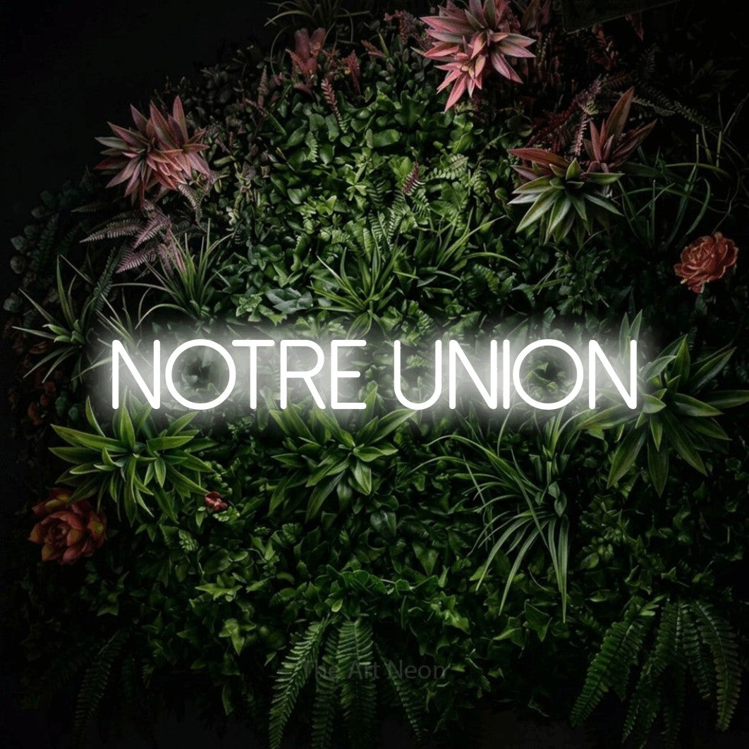 “Notre union” LED neon sign in cool white, with thin sans-serif lettering, shown against a flowering plant wall.