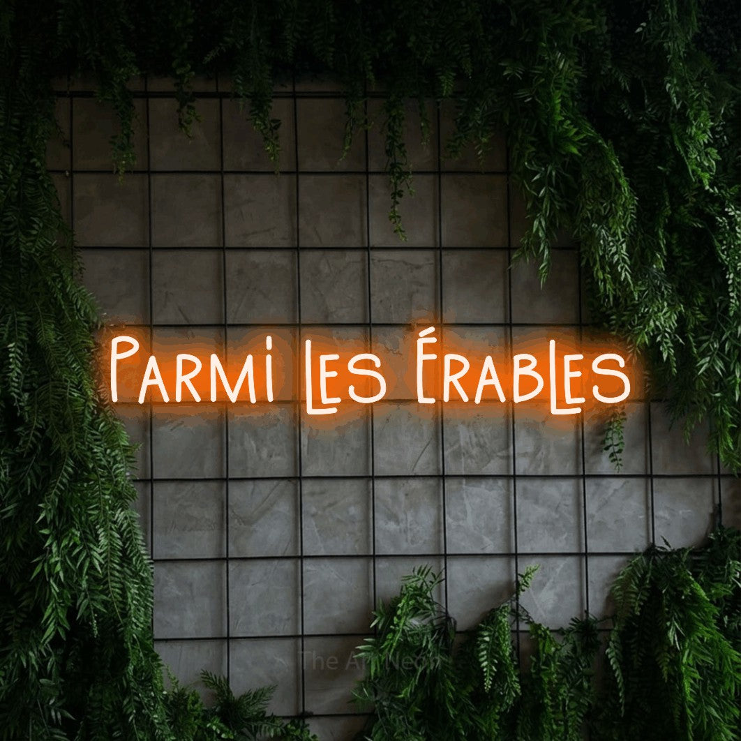 “Parmi les érables” LED neon sign in orange, with narrow hand-drawn lettering, shown against an ivy-covered concrete grid.