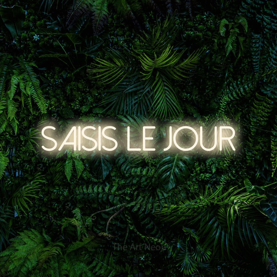 “Saisis le jour” LED neon sign in warm white, with thin sans-serif lettering, shown against dense tropical foliage.