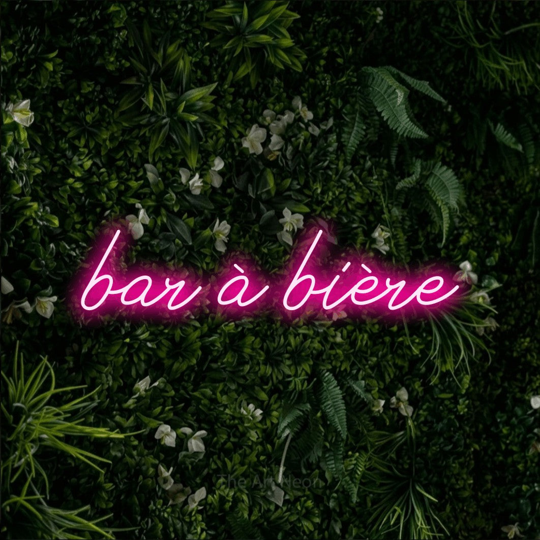 “Bar à bière” LED neon sign in hot pink, with cursive lettering, shown against a dense green plant wall.