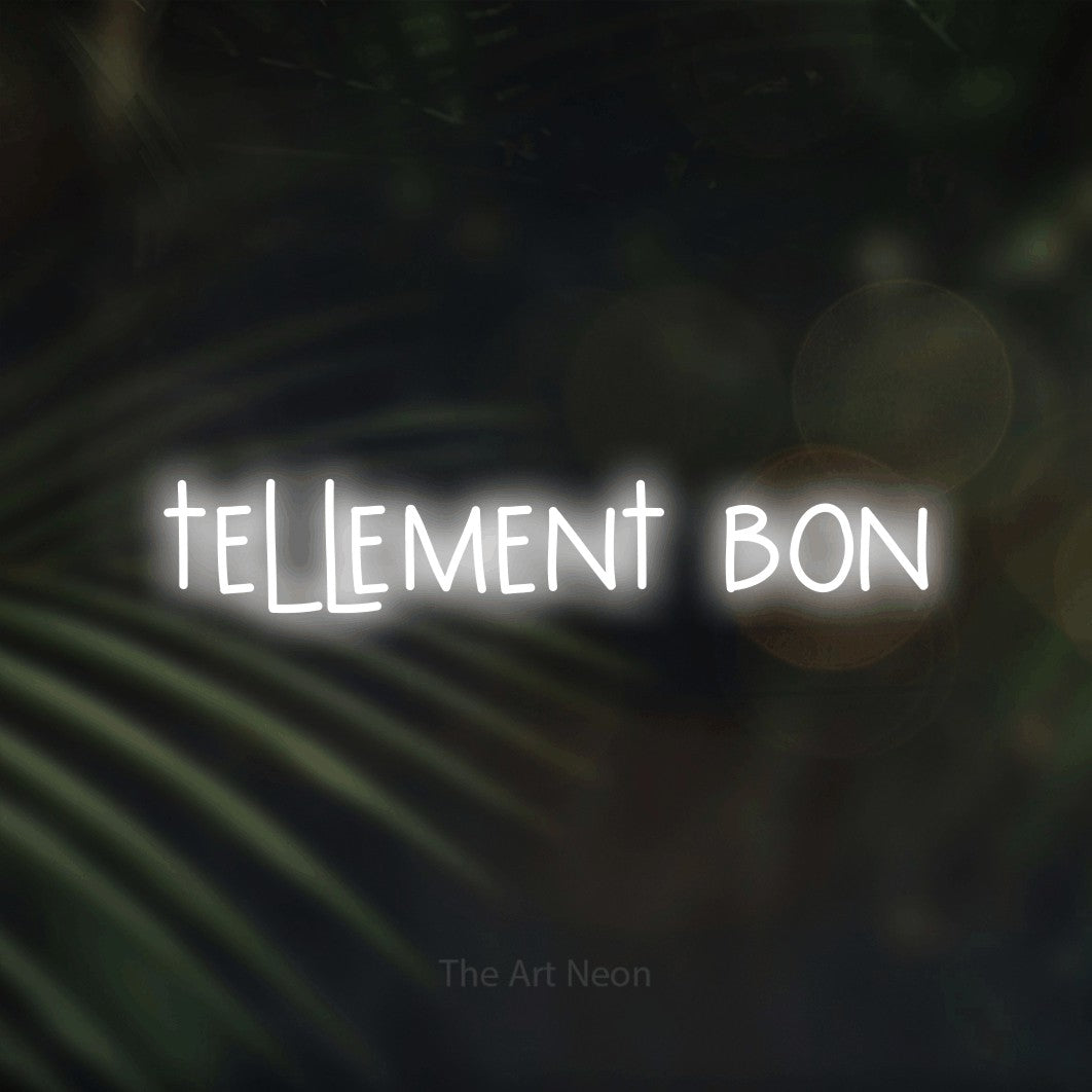“Tellement bon” LED neon sign in cool white, with narrow hand-drawn lettering, shown against a blurred palm and bokeh-light backdrop.