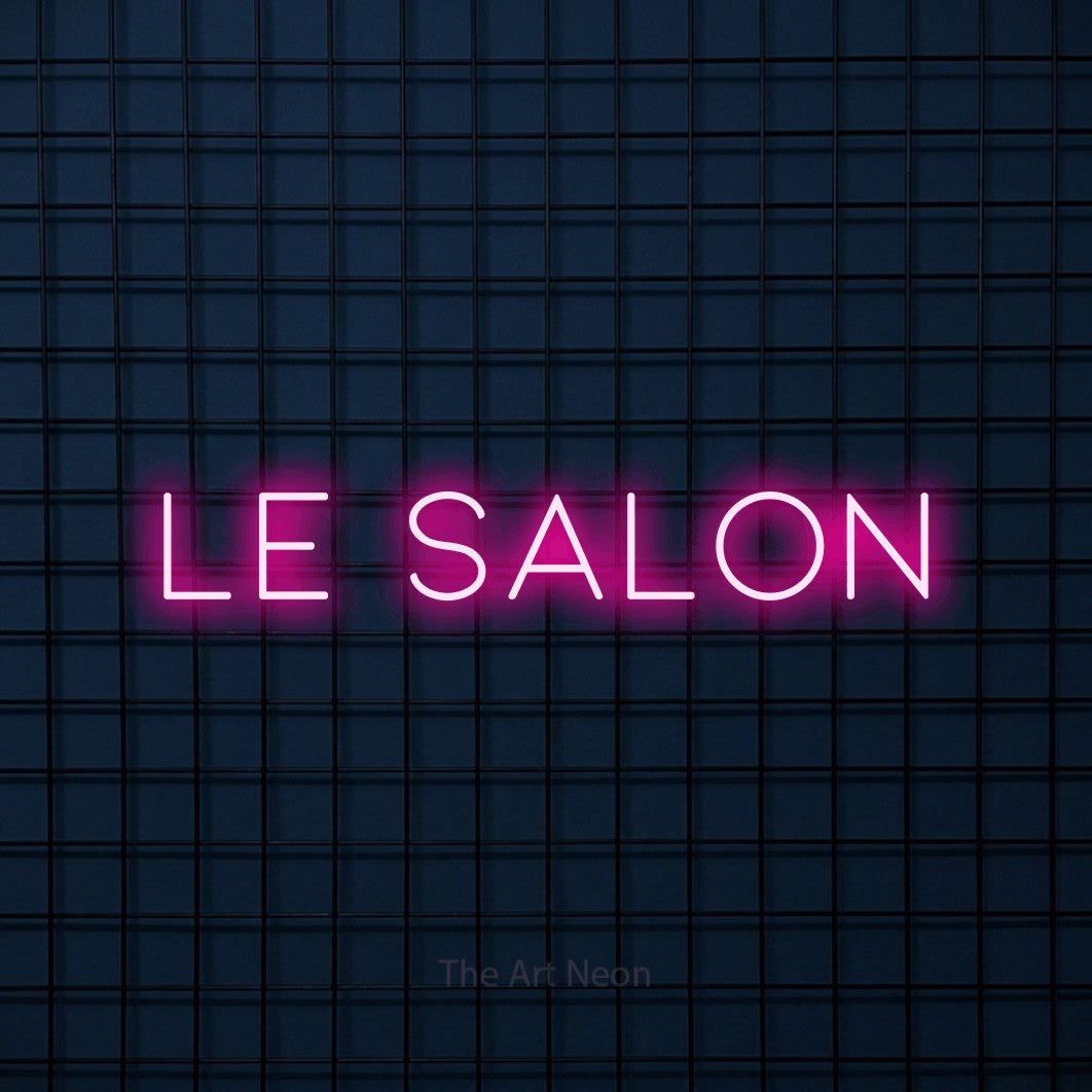 Décoration murale en néon LED « Le salon » en rose vif, en lettres fines et espacées, installée sur une grille bleu foncé, pour un salon de beauté.