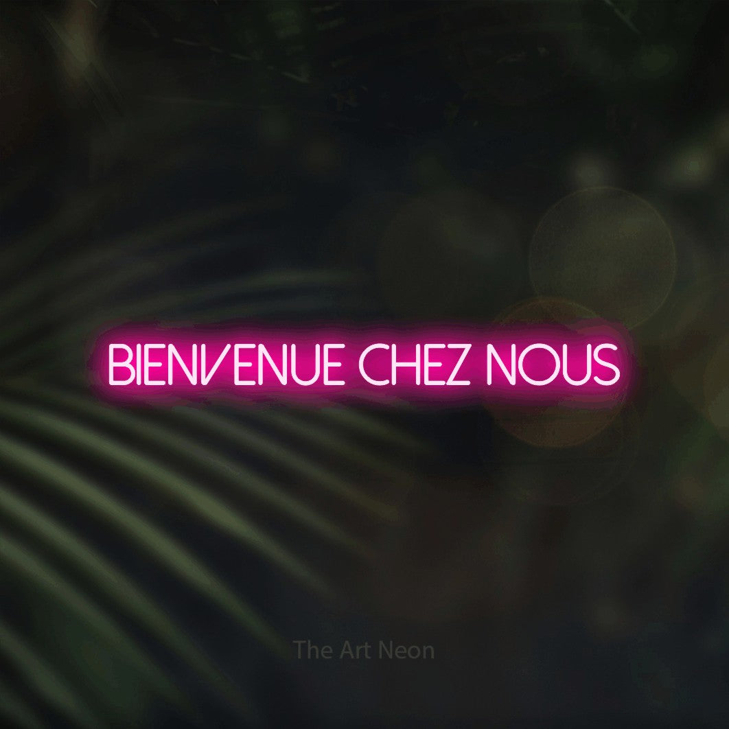 “Bienvenue chez nous” LED neon sign in hot pink, with thin sans-serif lettering, shown against a blurred palm and bokeh-light backdrop.