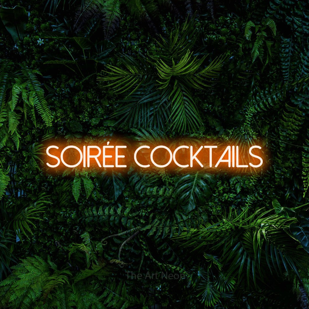 “Soirée cocktails” LED neon sign in orange, with thin sans-serif lettering, shown against dense tropical foliage.
