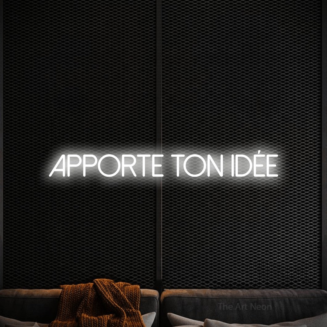 “Apporte ton idée” LED neon sign in cool white, with thin sans-serif lettering, shown against a modern dark-toned seating area.