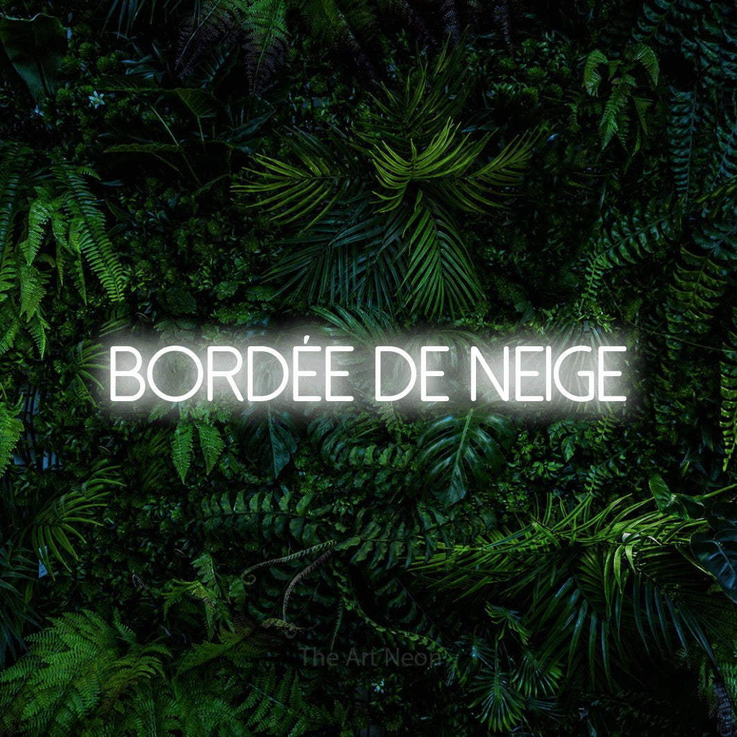 Composition en néon LED « Bordée de neige » en blanc froid, en lettres fines sans empattement, mise en valeur devant un feuillage tropical dense, pour un décor canadien.