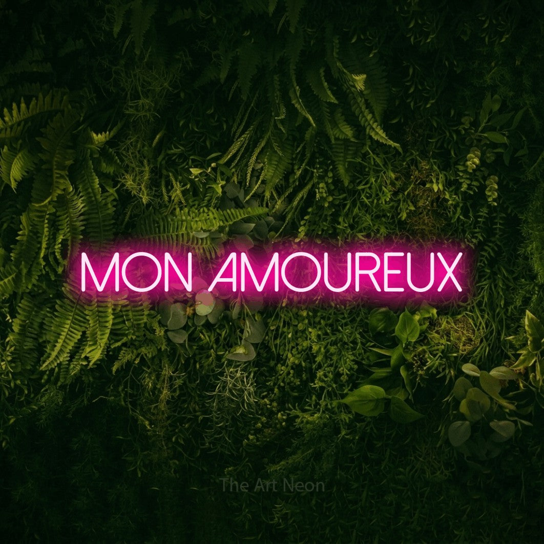 “Mon amoureux” LED neon sign in hot pink, with thin sans-serif lettering, shown against a dark moss and forest backdrop.
