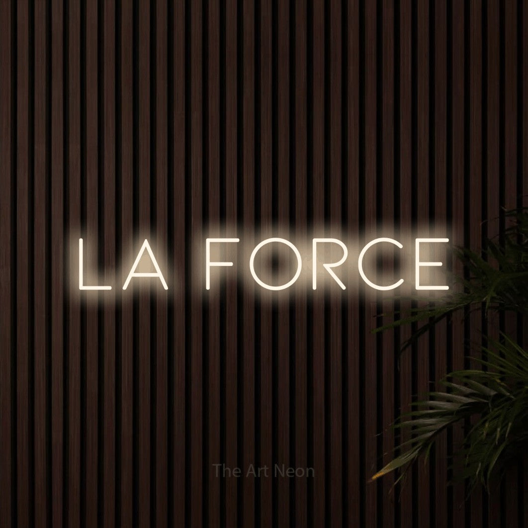 “La force” LED neon sign in warm white, with thin, widely spaced lettering, shown against dark wooden wall slats.
