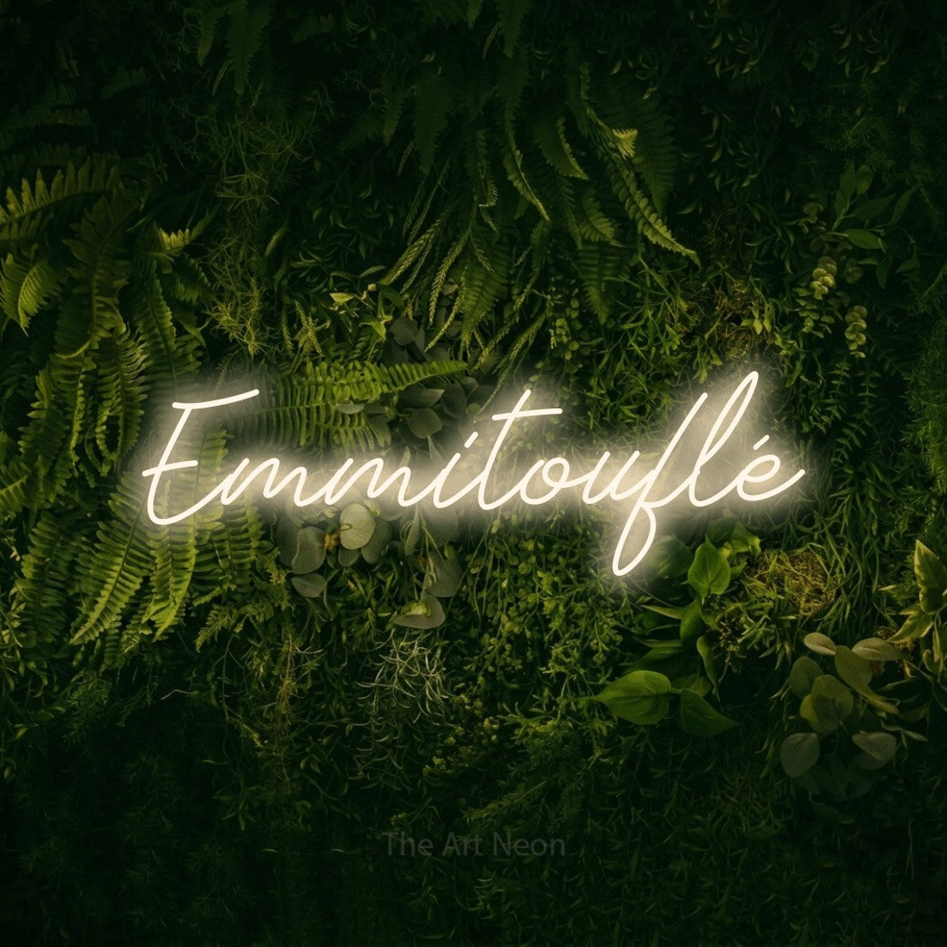 “Emmitouflé” LED neon sign in warm white, with cursive lettering, shown against a dark moss and forest backdrop.
