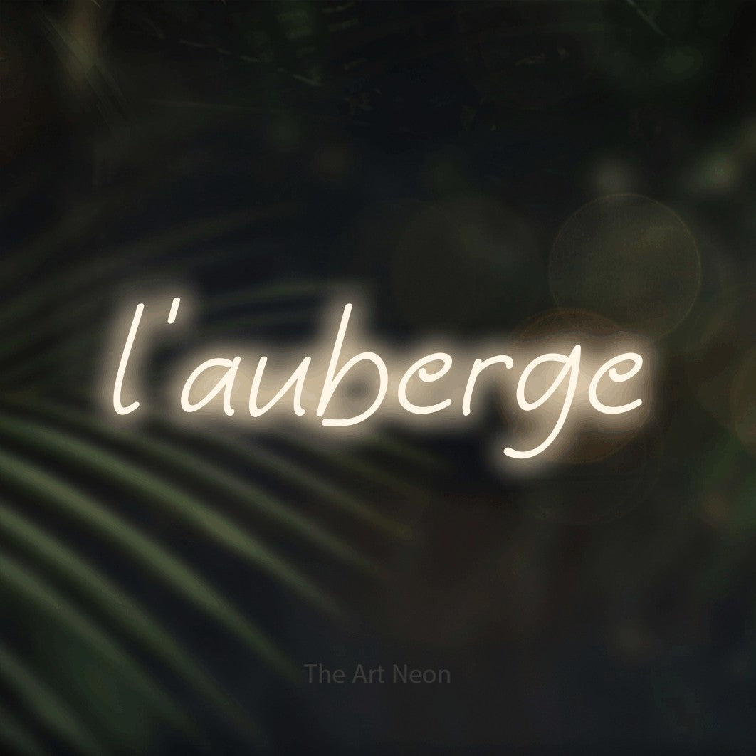 “L'auberge” LED neon sign in warm white, with slanted handwritten lettering, shown against a blurred palm and bokeh-light backdrop.