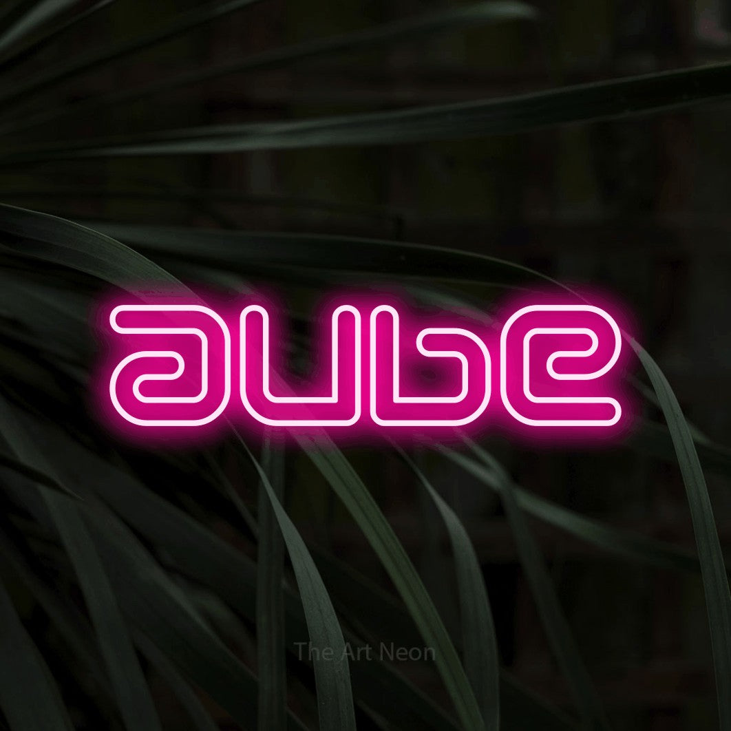 “Aube” LED neon sign in hot pink, with futuristic double-line lettering, shown against a close-up of dark foliage.