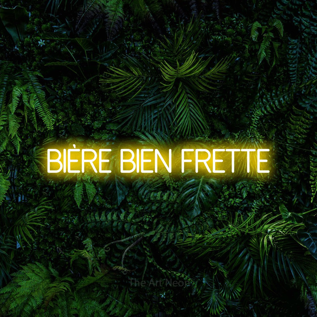 Enseigne néon LED « Bière bien frette » en jaune, en lettres fines sans empattement, présentée devant un feuillage tropical dense, pour un bar à la maison.