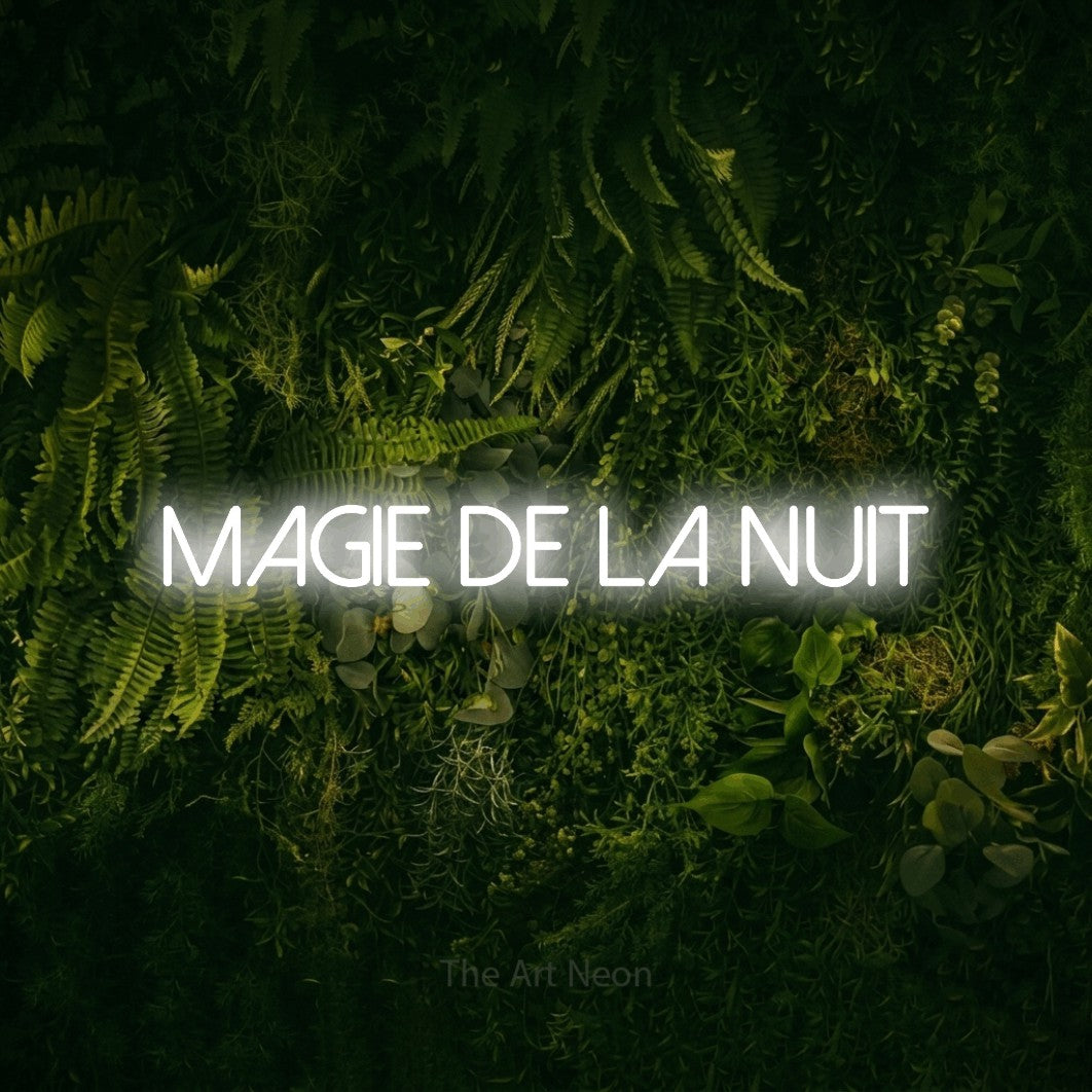 “Magie de la nuit” LED neon sign in cool white, with thin sans-serif lettering, shown against a dark moss and forest backdrop.