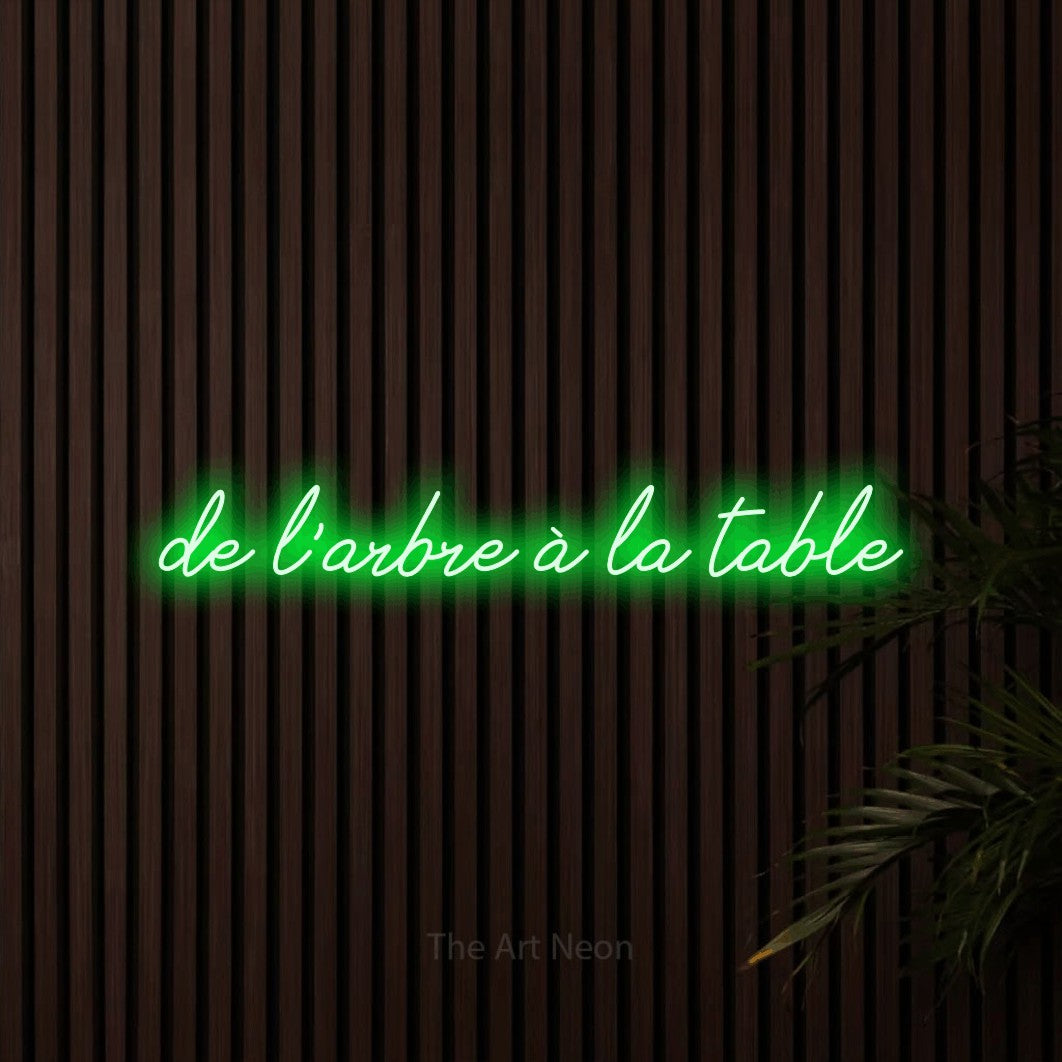 “De l'arbre à la table” LED neon sign in green, with cursive lettering, shown against dark wooden wall slats.