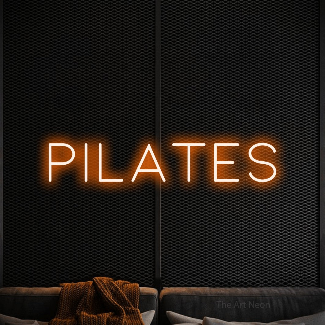 “Pilates” LED neon sign in orange, with thin, widely spaced lettering, shown against a modern dark-toned seating area.