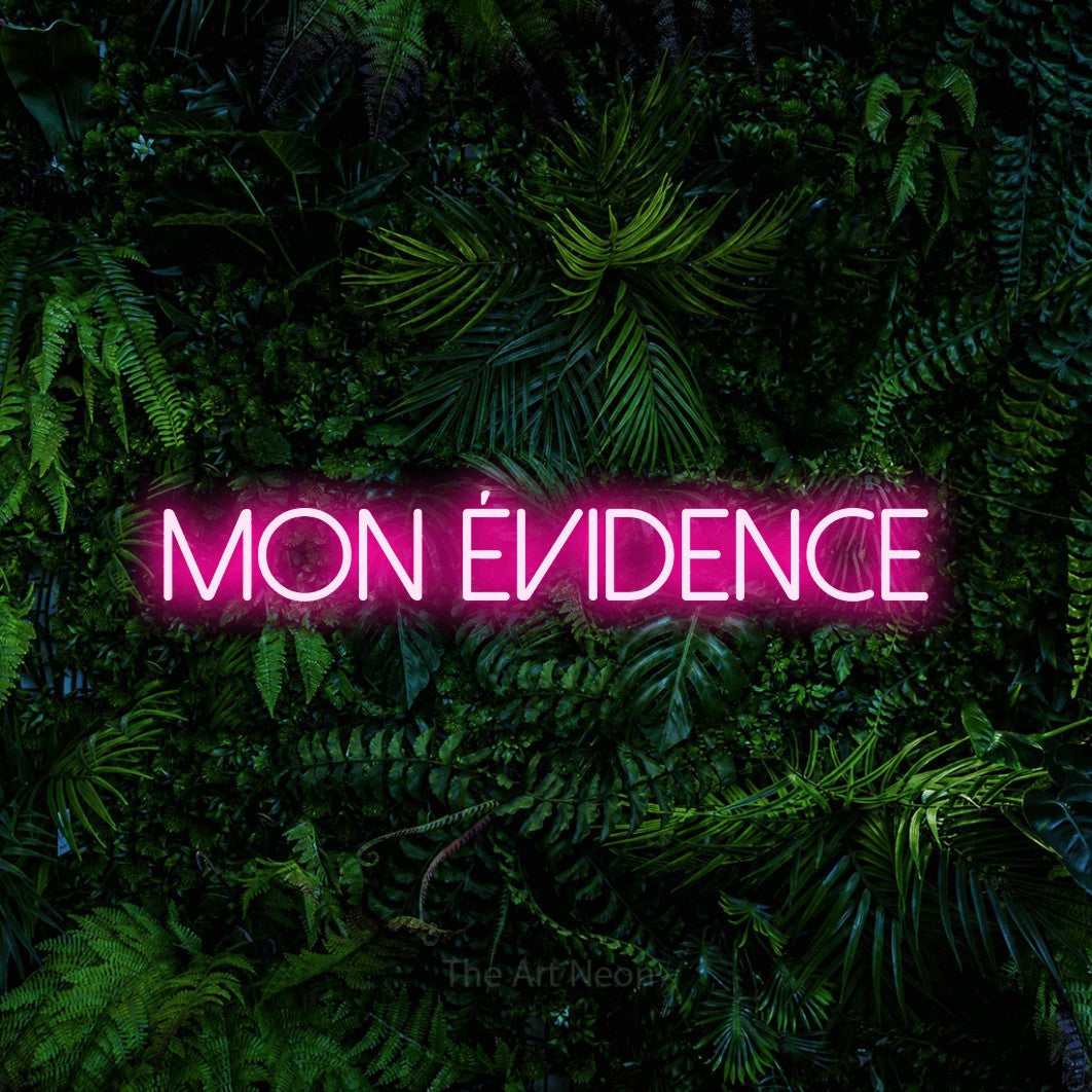 “Mon évidence” LED neon sign in hot pink, with thin sans-serif lettering, shown against dense tropical foliage.