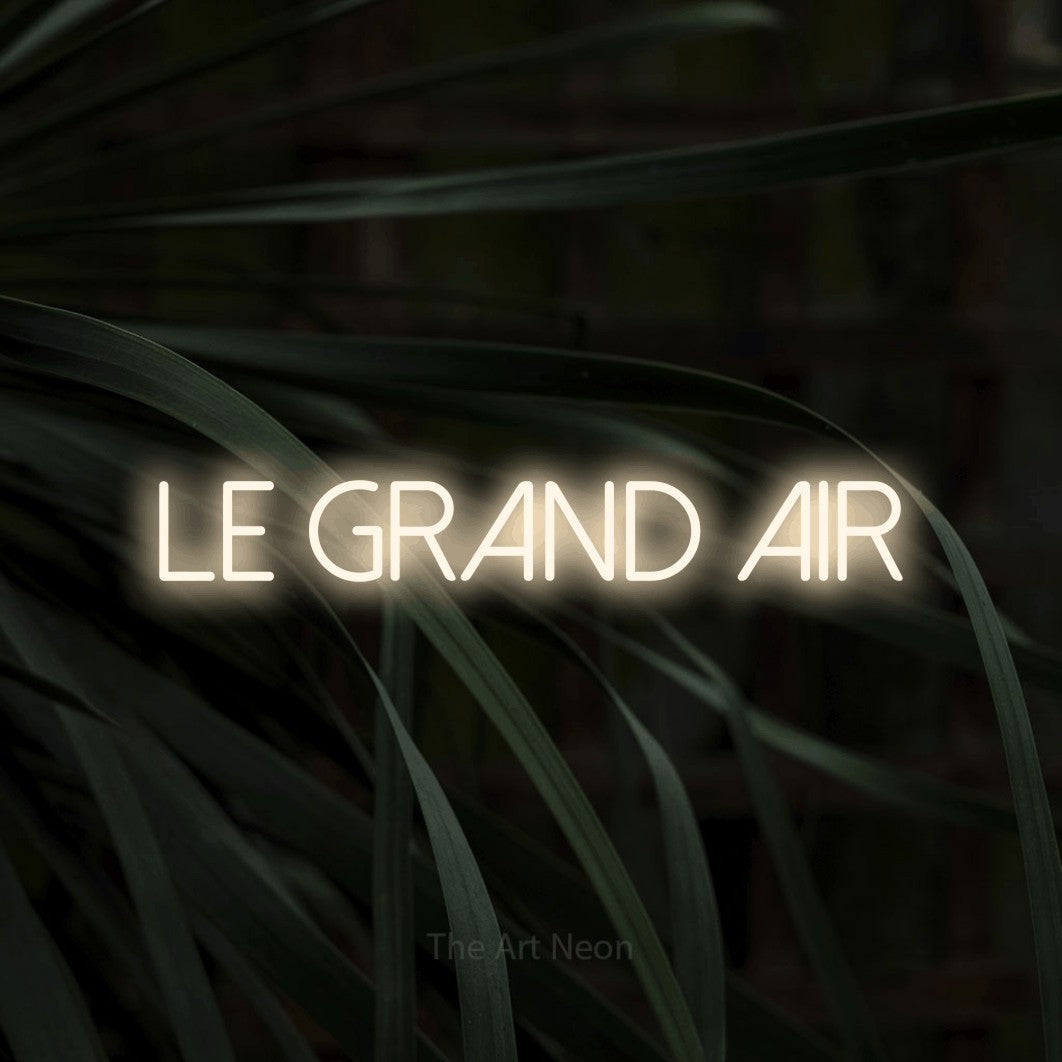 Lettrage en néon LED « Le grand air » en blanc chaud, en lettres fines sans empattement, présenté sur un feuillage sombre en gros plan, pour un décor inspiré de la nature.