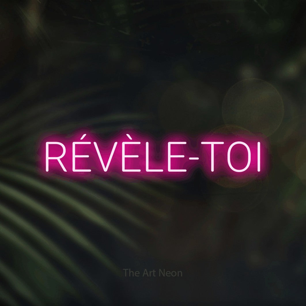 Lettrage en néon LED « Révèle-toi » en rose vif, en lettres sans empattement arrondies, présenté sur un fond flou de palmiers et de lumières bokeh, pour un salon de beauté.
