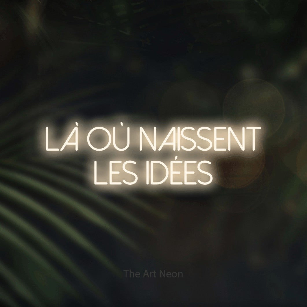 “Là où naissent les idées” LED neon sign in warm white, with thin sans-serif lettering across 2 lines, shown against a blurred palm and bokeh-light backdrop.