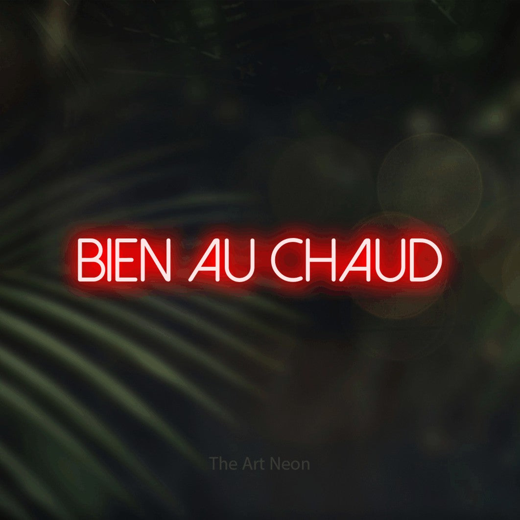 “Bien au chaud” LED neon sign in red, with thin sans-serif lettering, shown against a blurred palm and bokeh-light backdrop.