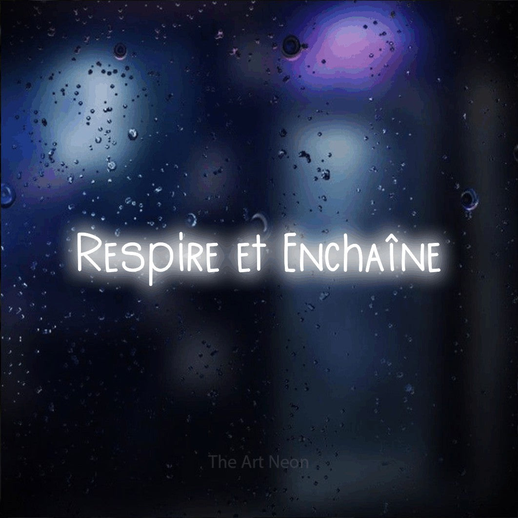 Enseigne néon LED « Respire et enchaîne » en blanc froid, en lettres étroites dessinées à la main, présentée sur une vitre aux reflets bleus et violets, pour un espace d’entraînement.