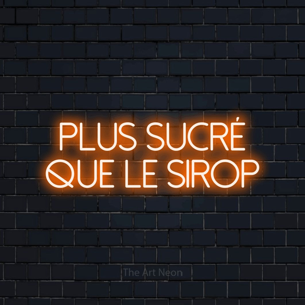 “Plus sucré que le sirop” LED neon sign in orange, with thin sans-serif lettering across 2 lines, shown against a dark navy brick wall.
