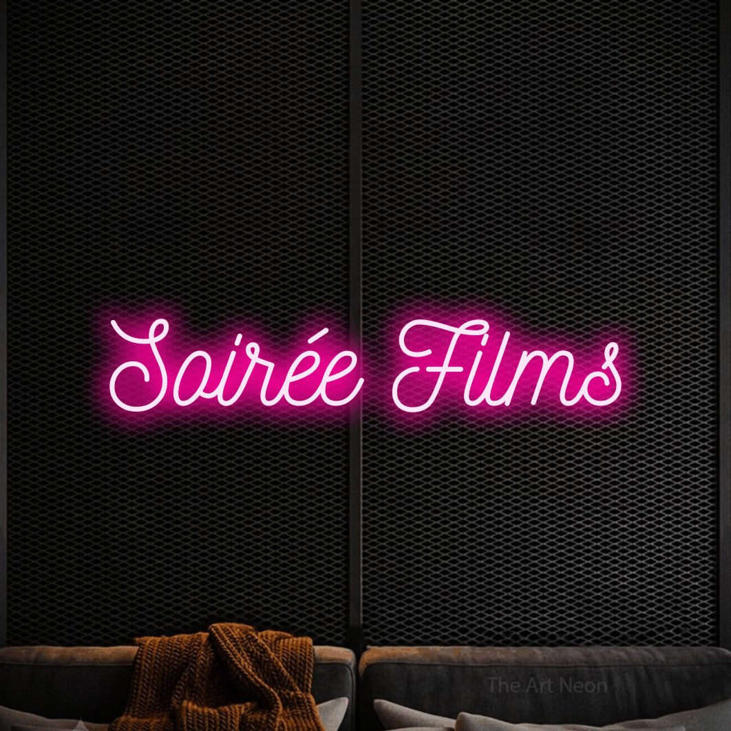 “Soirée films” LED neon sign in hot pink, with ornate cursive lettering, shown against a modern dark-toned seating area.