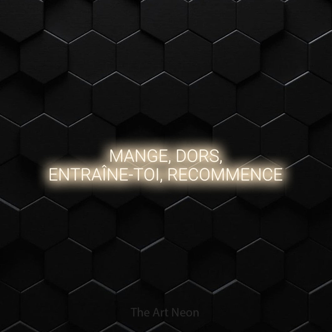 Décoration murale en néon LED « Mange, dors, entraîne-toi, recommence » sur deux lignes en blanc chaud, en lettres sans empattement arrondies, installée sur un mur de carreaux hexagonaux noirs, pour un espace d’entraînement.