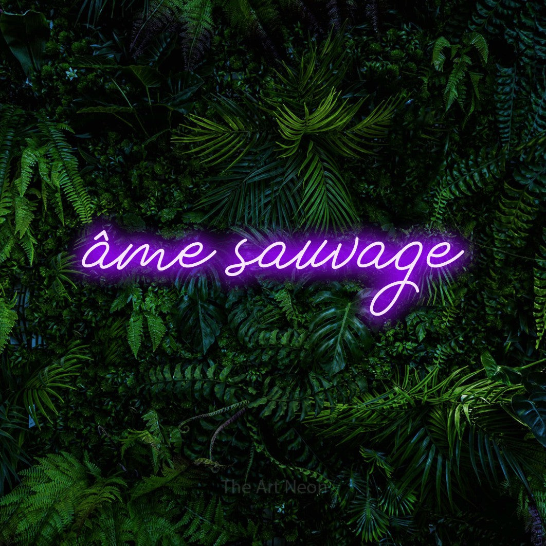 “Âme sauvage” LED neon sign in purple, with cursive lettering, shown against dense tropical foliage.