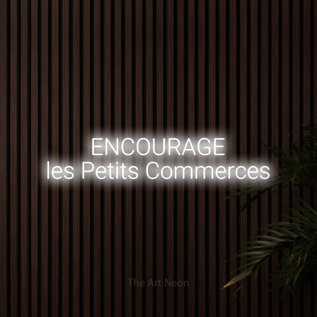 “Encourage les petits commerces” LED neon sign in cool white, with rounded sans-serif lettering across 2 lines, shown against dark wooden wall slats.