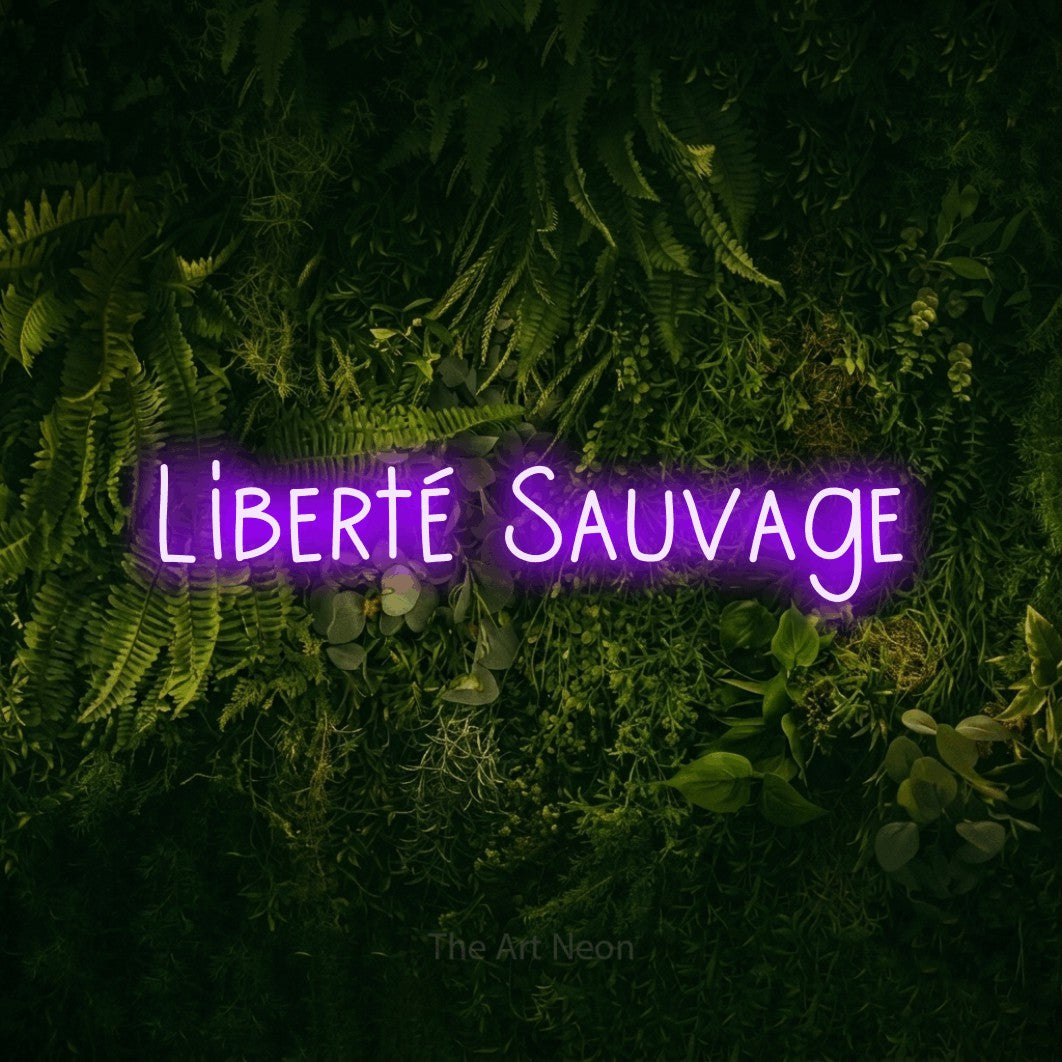“Liberté sauvage” LED neon sign in purple, with narrow hand-drawn lettering, shown against a dark moss and forest backdrop.
