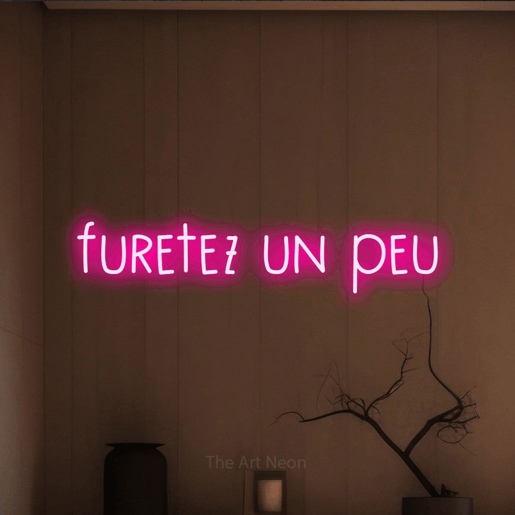 “Furetez un peu” LED neon sign in hot pink, with narrow hand-drawn lettering, shown against a simple earth-toned interior.