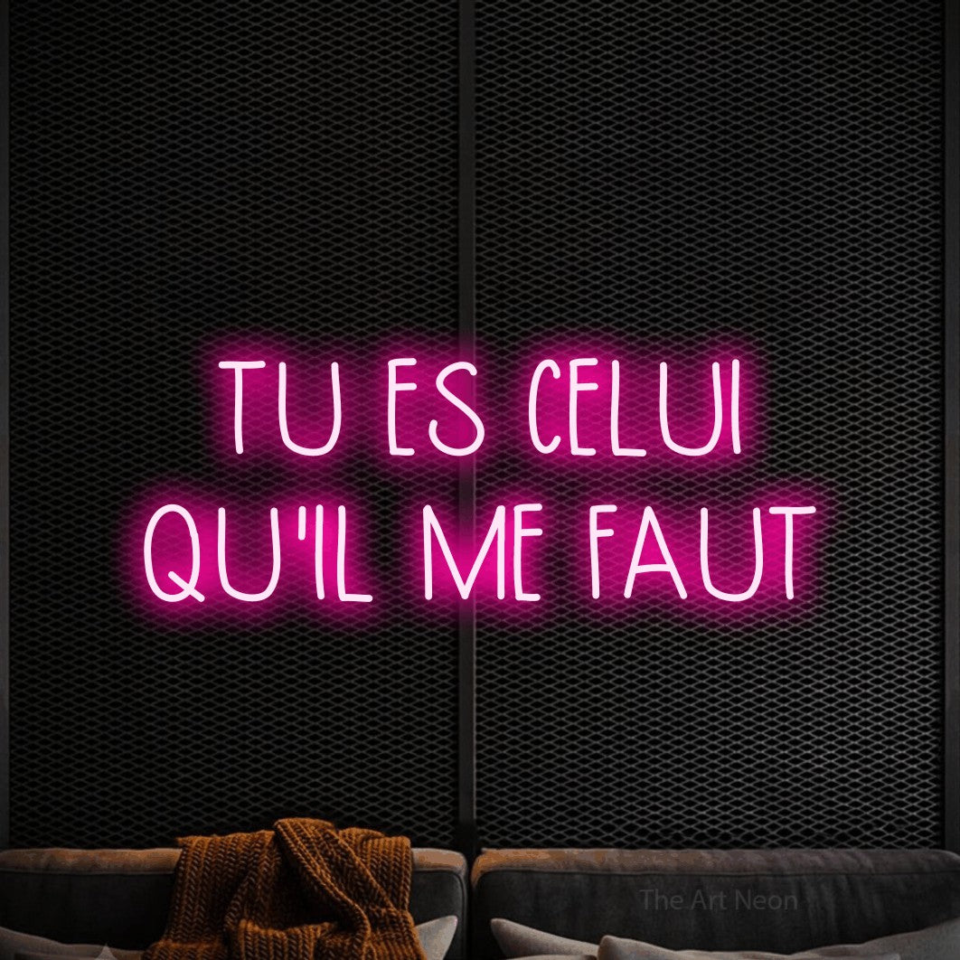 “Tu es celui qu'il me faut” LED neon sign in hot pink, with narrow hand-drawn lettering across 2 lines, shown against a modern dark-toned seating area.
