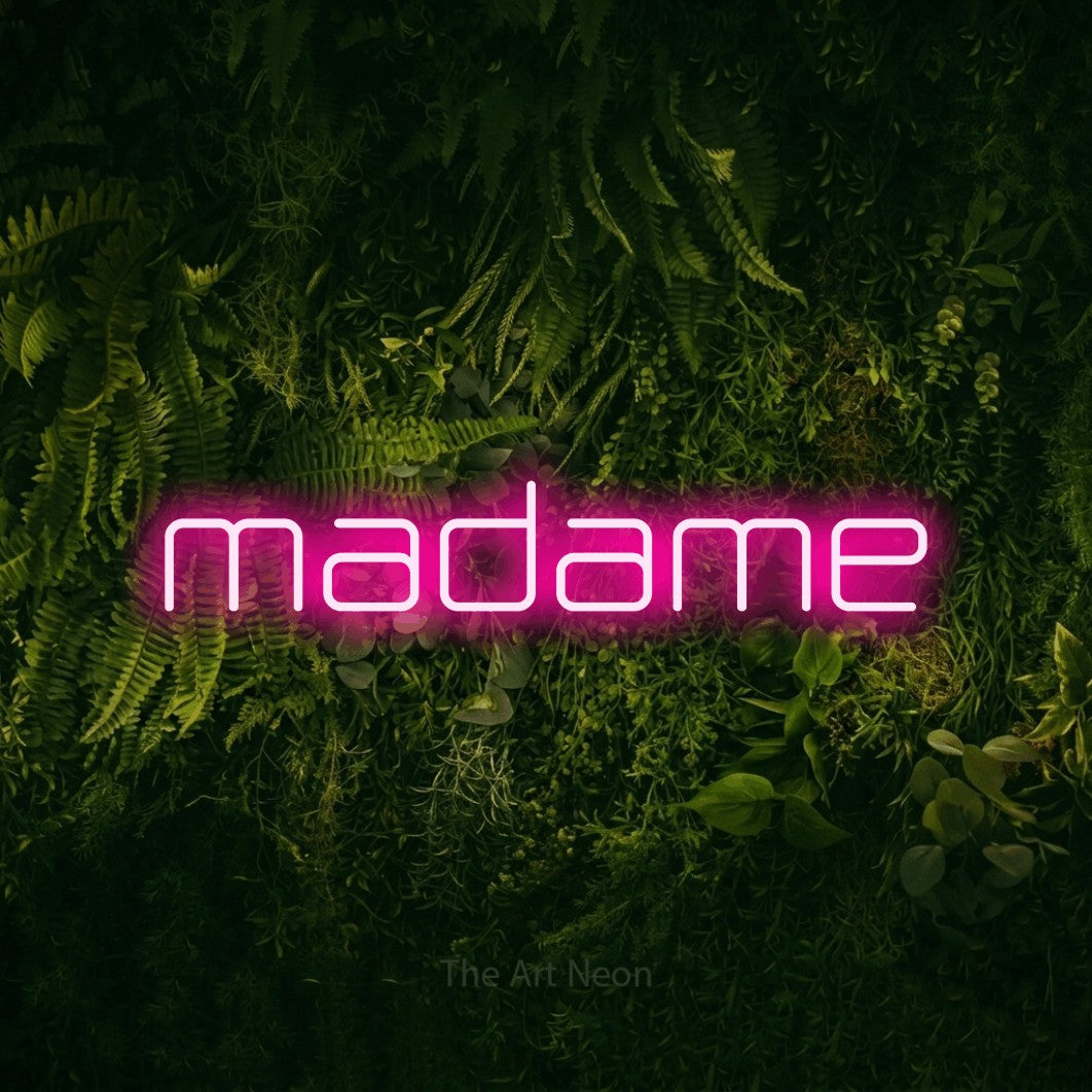 Lettrage en néon LED « Madame » en rose vif, en lettres géométriques aux angles arrondis, présenté sur un fond sombre de mousse et de forêt, pour une réception de mariage.