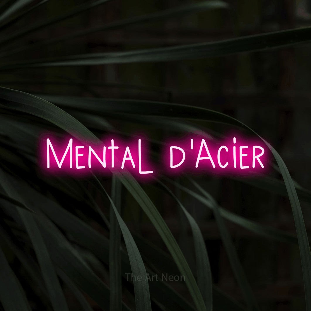 “Mental d'acier” LED neon sign in hot pink, with narrow hand-drawn lettering, shown against a close-up of dark foliage.