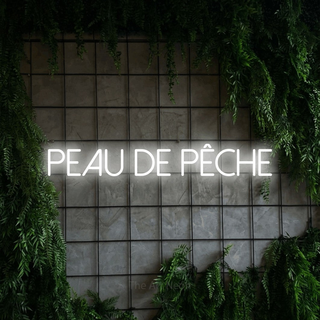 Lettrage en néon LED « Peau de pêche » en blanc froid, en lettres fines sans empattement, présenté sur une grille de béton couverte de lierre, pour un salon de beauté.
