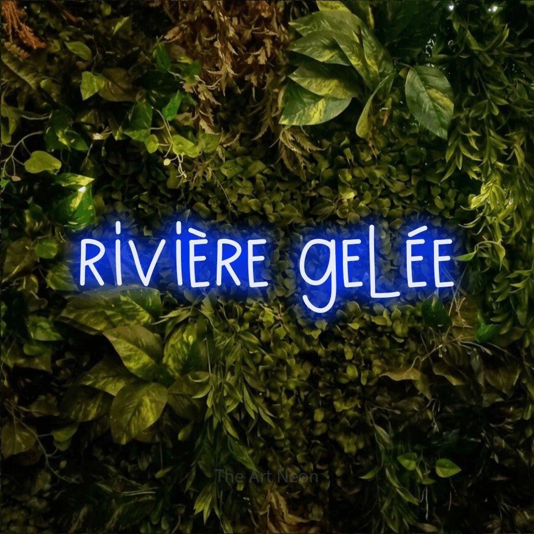 “Rivière gelée” LED neon sign in blue, with narrow hand-drawn lettering, shown against bright green and yellow foliage.