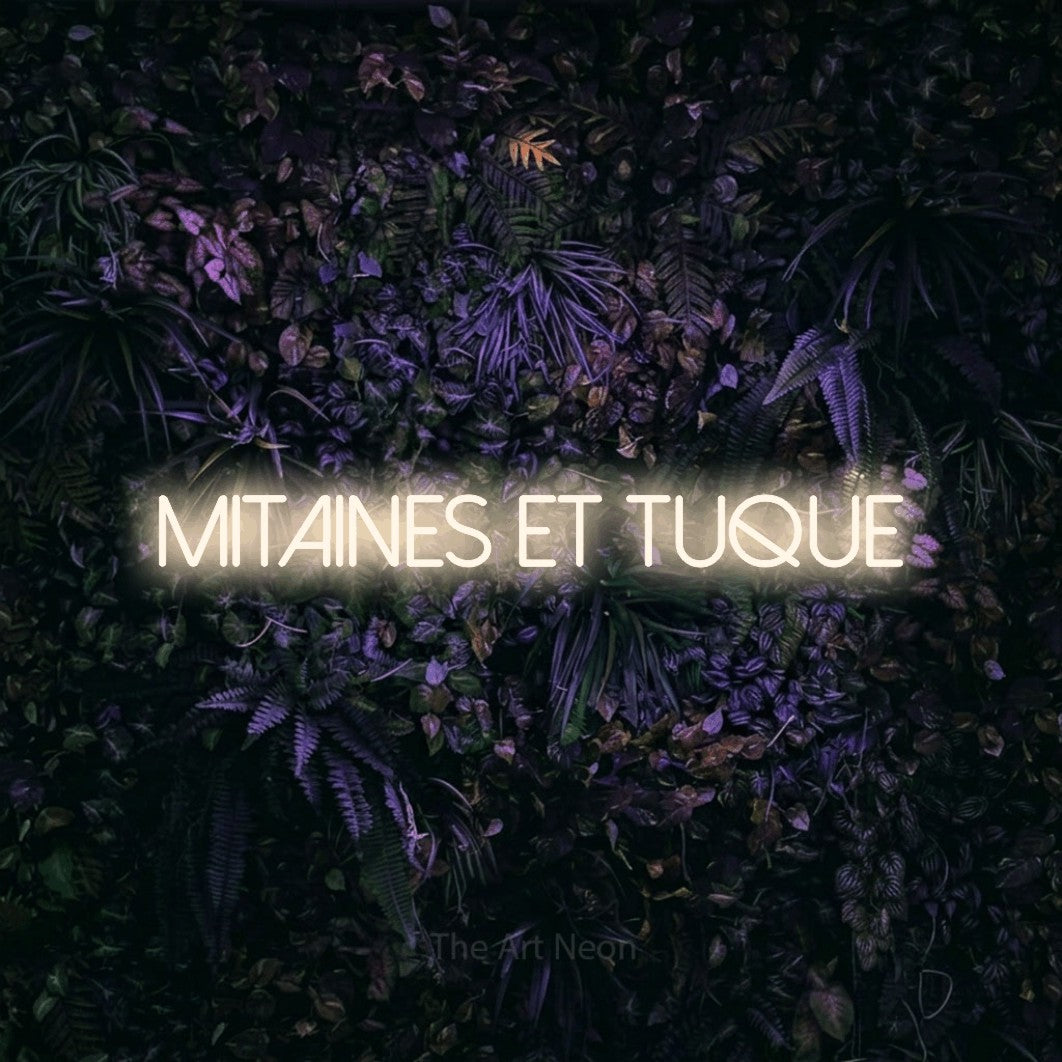 Décoration murale en néon LED « Mitaines et tuque » en blanc chaud, en lettres fines sans empattement, installée sur un mur sombre aux fleurs violettes, pour un décor canadien.