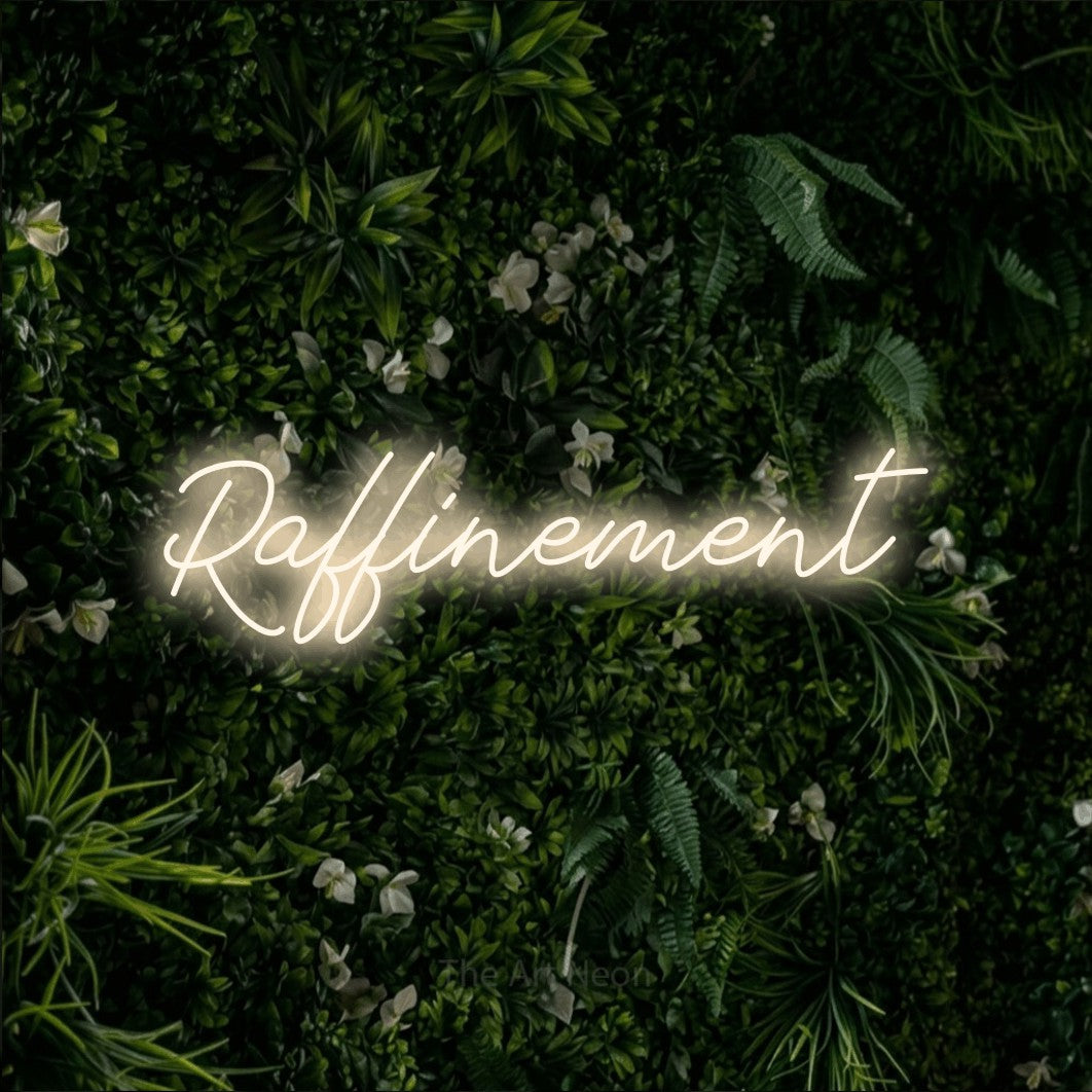 “Raffinement” LED neon sign in warm white, with cursive lettering, shown against a dense green plant wall.